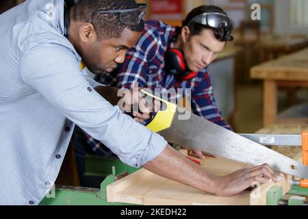 two men in carpentry workshop one using handsaw Stock Photo