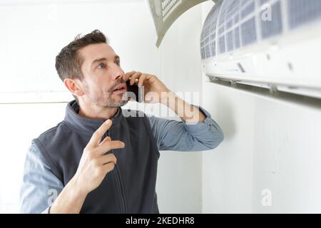 repairman contractor using the phone while repairing heating panel Stock Photo