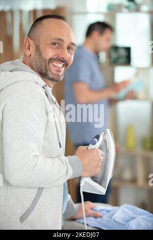 man ironing shirt on ironing board with steaming blue iron Stock Photo