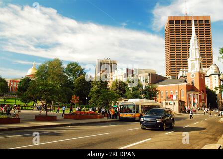 Traffic moves along Tremont Street, next to Boston Common with the Park Street Church and the downtown city in the background Stock Photo