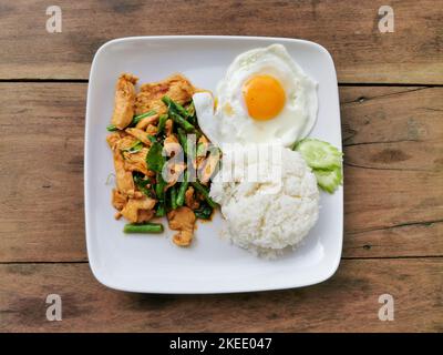Pad prik gaeng moo or stir fried red curry pork with white rice on white plate with wood background. Thai street food in Thailand. Stock Photo