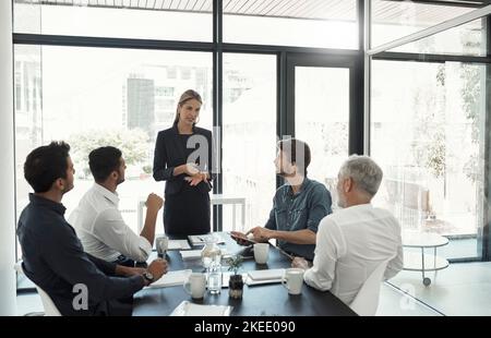 Talking business in the boardroom. a businesswoman talking to colleagues sitting around a table in an boardroom. Stock Photo