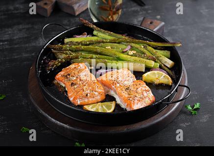 Delicious baked salmon with asparagus, lemon slices and spices on dark table. Stock Photo