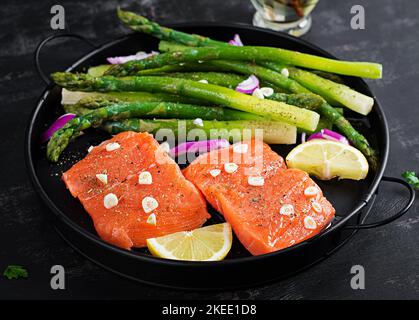 Prepared for baking salmon with asparagus, lemon slices and spices on dark table. Stock Photo