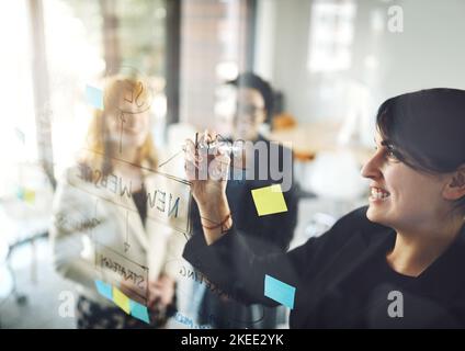 Shes got some ideas to share. three businesswoman using a glass wipe board during a brainstorming session. Stock Photo