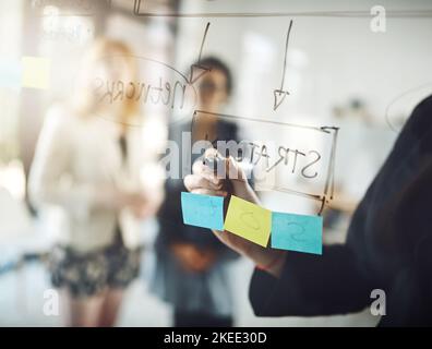 Focused on the end goal. three businesswoman using a glass wipe board during a brainstorming session. Stock Photo