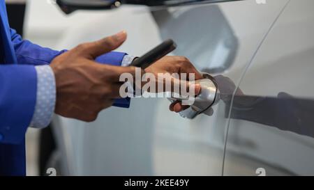 Black salesman opens car using app on mobile phone Stock Photo