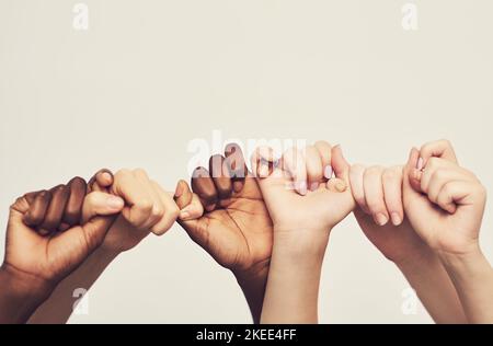 Sticking together. a group of unrecognizable people holding one anothers thumbs in a single line. Stock Photo