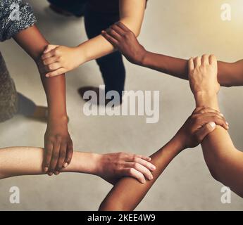 There is strength in unity. High angle shot of a group of unrecognizable people holding one anothers arms to form a circle. Stock Photo