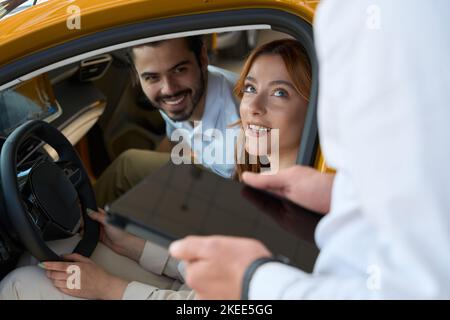 Joyous auto dealership customers communicating with sales consultant Stock Photo