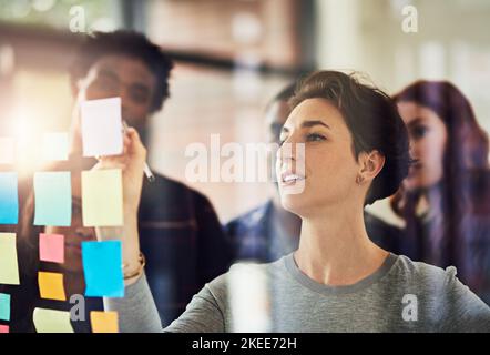 Productive planning. coworkers using sticky notes on a glass wall during an office meeting. Stock Photo