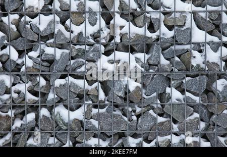 Gabion, texture, background. Snow covered gabion net and stone fencing design. New technologies in the manufacture of retaining walls and fences