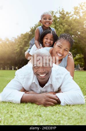 Family, children and park with a woman, man and daughter siblings lying on grass together outdoor in summer. Portrait, face and pile with a mother Stock Photo