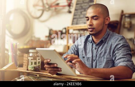 Organizing his tasks on his tablet. a young entrepreneur using a digital tablet in his store. Stock Photo