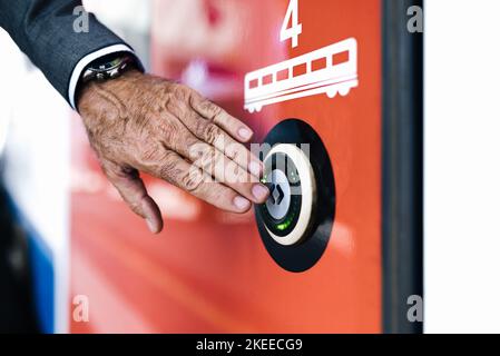 Close-up of senior businessman pushing open door button. Convenient technology on modern subway train. He is traveling by train at railroad station. Stock Photo
