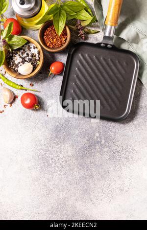 Food cooking background on gray background with grill pan. Empty grill skillet, vegetables, spices and herbs on stone table.  View from above. Copy sp Stock Photo