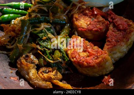 Indonesian food called Tempe Penyet with spicy chili sauce and some vegetables in a stone mortar Stock Photo
