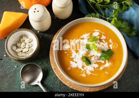Vegetarian pumpkin and carrot cream soup with cream and pumpkin seeds on a stone tabletop. Comfort food, fall and winter healthy slow food concept. Stock Photo