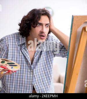 The young handsome man enjoying painting at home Stock Photo