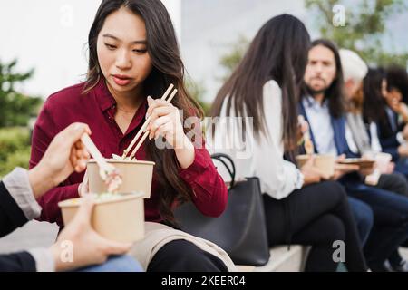 Multiethnic business people doing lunch break outdoor from office building - Focus on asian girl face Stock Photo