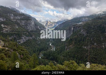 Valley in Yosemeti National Park with conifers, low clouds, cloudy sky and patches of fog, California, USA Stock Photo