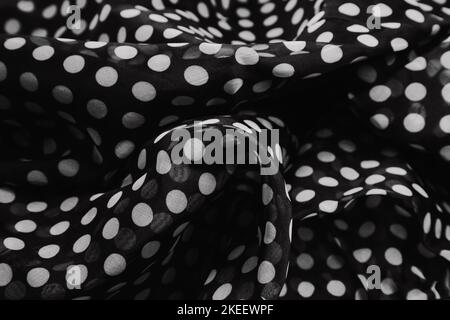 Gathered and folded texture of black and white color polka dot printed fabric. Ripples and folds form a wavy black texture. Seamless pattern of cloth. Stock Photo