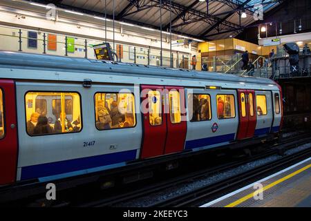 London Underground (the Tube); a train on the District Line stopping at Earls Court station at dusk, the carriage lights showing the passengers inside Stock Photo