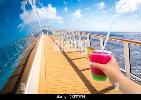 Hand holding a glass with cocktail on a deck of cruise ship with ocean on background