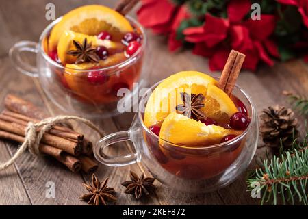 Mulled wine with orange slices, cranberries and spices on rustic wooden table and holiday decoration in background Stock Photo