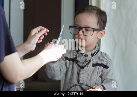 a little boy with glasses and a stel in his hand, looking at something on the table next to him Stock Photo