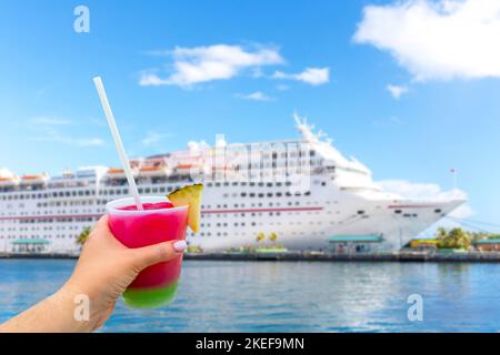 Hand holding a glass with cocktail with cruise ship in a port on background