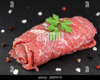 single raw unfilled beef roulade with salt and peper on black slate board, traditional german food Stock Photo