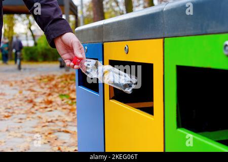 Throwing a plastic bottle into a color-coded waste collection bin placed in the public park. Stock Photo