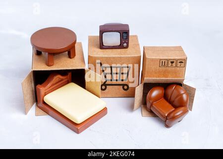 Tiny shipping boxes and miniature furniture figurines isolated on gray background. Moving old furniture vs buying new essentials. Stock Photo