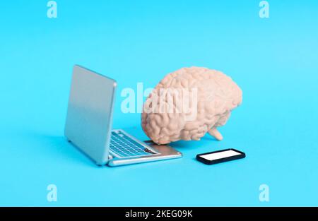 Toy human brain placed by miniature laptop and smartphone figurines isolated on blue background. Stock Photo