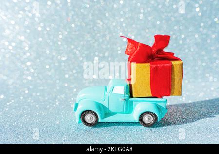 Miniature toy pickup truck carrying a large gift box against a glittering Christmas background. Stock Photo