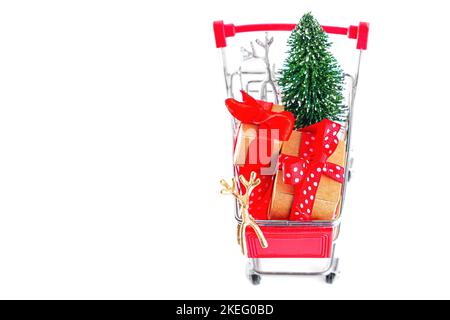 Miniature supermarket push cart with tiny new year tree, toy christmas deers and wrapped gift boxes isolated on white background with copy space. Stock Photo