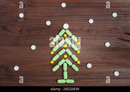 Decorated Christmas tree flat lay made from pills on a wooden background. Creative sick at Christmas concept. Stock Photo
