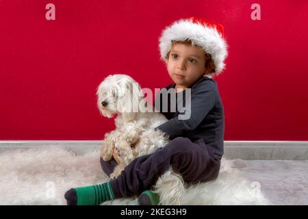 photo of boy with santa claus hat hugging his puppy Stock Photo