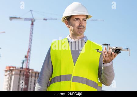Man launches a quadcopter. An engineer flies a drone next to a construction site. Concept - construction observation with a drone.  Construction crane Stock Photo
