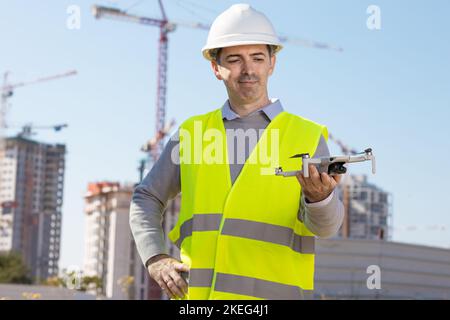 Man launches a quadcopter. An engineer flies a drone next to a construction site. Concept - construction observation with a drone.  Construction crane Stock Photo