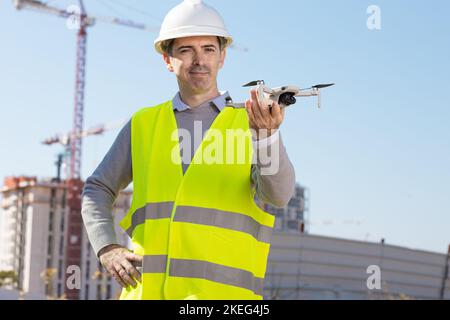 Man launches a quadcopter. An engineer flies a drone next to a construction site. Concept - construction observation with a drone.  Construction crane Stock Photo