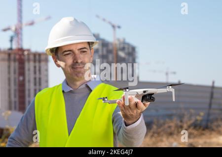 Man launches a quadcopter. An engineer flies a drone next to a construction site. Concept - construction observation with a drone.  Construction crane Stock Photo
