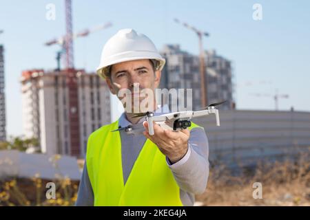 Man launches a quadcopter. An engineer flies a drone next to a construction site. Concept - construction observation with a drone.  Construction crane Stock Photo