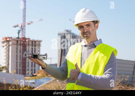 Man launches a quadcopter. An engineer flies a drone next to a construction site. Concept - construction observation with a drone.  Construction crane Stock Photo