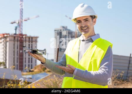 Man launches a quadcopter. An engineer flies a drone next to a construction site. Concept - construction observation with a drone.  Construction crane Stock Photo