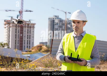 Man launches a quadcopter. An engineer flies a drone next to a construction site. Concept - construction observation with a drone.  Construction crane Stock Photo
