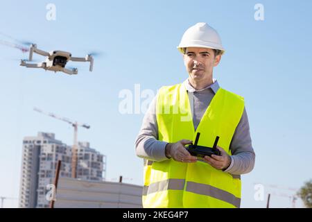 Man launches a quadcopter. An engineer flies a drone next to a construction site. Concept - construction observation with a drone.  Construction crane Stock Photo