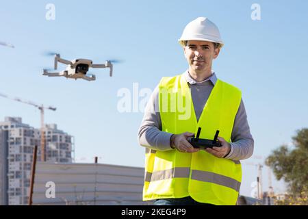 Man launches a quadcopter. An engineer flies a drone next to a construction site. Concept - construction observation with a drone.  Construction crane Stock Photo