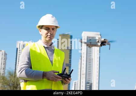 Man launches a quadcopter. An engineer flies a drone next to a construction site. Concept - construction observation with a drone.  Construction crane Stock Photo